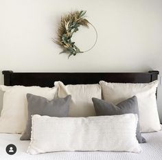 a white bed topped with pillows and a wreath on the wall above it's headboard