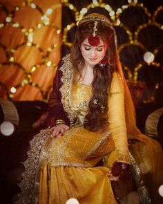 a woman in a yellow dress sitting on a chair with lights around her and wearing a red head piece