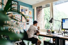 a man sitting at a desk in front of a large window with lots of pictures on the wall