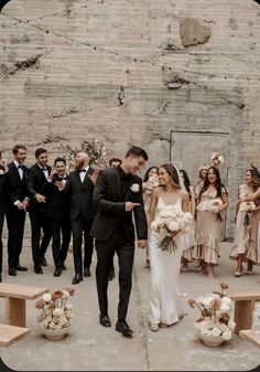 a bride and groom standing in front of a group of people wearing tuxedos