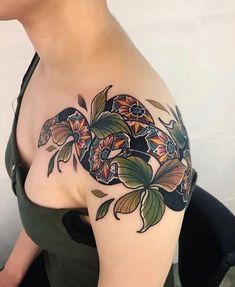 a woman's shoulder with flowers and leaves on her left arm, which is covered in black ink