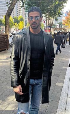 a man in black jacket and jeans standing on sidewalk