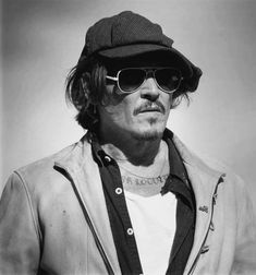 black and white photograph of a man with sunglasses on his face wearing a hat, jacket, and scarf