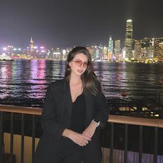 a woman standing in front of a body of water with a city skyline in the background