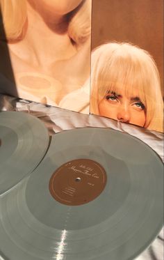 two silver records sitting on top of a table next to a poster with a woman's face