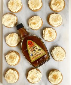 a bottle of syrup sitting on top of cupcakes next to some frosted cookies