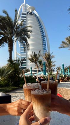 three people toasting with drinks in front of the burj hotel and palm trees