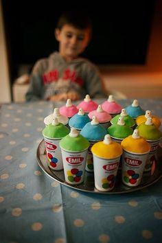 a child sitting at a table in front of a tray with cupcakes on it