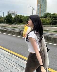 a woman walking down the street while holding a hot dog