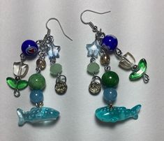 ❀ Handmade and one of a kind ❀ flower and sealife themed blue, green and silver wire wire earrings ❀ 18 round, star, and tulip  shaped beads ❀Great gift for friend, family member, or anyone who enjoys a little bit of joy and whimsy ❀ Dimensions: 3 1/2" length 2" wide (both earrings set side by side) Whimsical Blue Nickel-free Earrings, Fun Blue Round Beads Jewelry, Blue Whimsical Earrings For Gifts, Fun Blue Round Beaded Jewelry, Fun Handmade Blue Jewelry, Whimsical Blue Round Jewelry, Handmade Blue-green Jewelry Gift, Whimsical Round Blue Jewelry, Green Ocean-inspired Nickel-free Jewelry