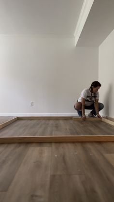 a man kneeling down on top of a hard wood floor next to a white wall