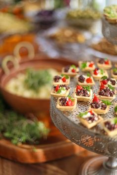 many small desserts are arranged on a silver platter with other food items in the background