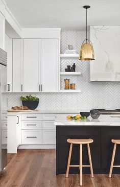 two stools sit in front of the kitchen island with marble backsplash and gold pendant lights