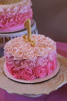 two tiered cakes with pink frosting and gold numbers on top, sitting on a table