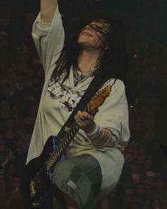 a woman with long black hair and piercings on her head holding a guitar in front of an audience