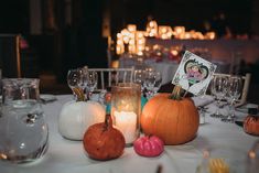 a table topped with lots of different types of candles and pumpkins next to wine glasses