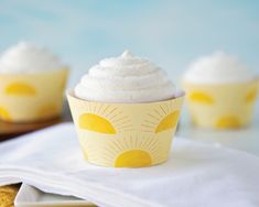 three cupcakes with white frosting and sun designs on them sitting on a napkin