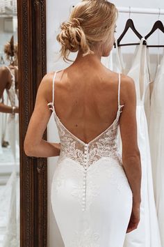 a woman standing in front of a mirror wearing a wedding dress with straps and open back