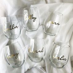 four wine glasses with gold lettering on them sitting on a white cloth covered bed sheet