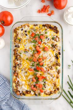 a casserole dish with cheese, tomatoes and other ingredients on a white table