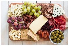 an assortment of cheeses, crackers, and grapes on a wooden platter