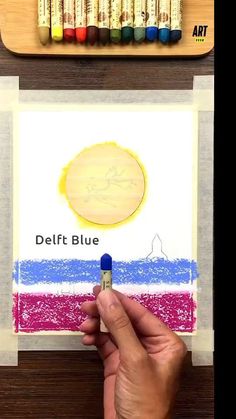 a person is holding a crayon pencil in their left hand and drawing on paper with the word delft blue