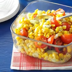 a glass bowl filled with corn and tomatoes on top of a red checkered napkin