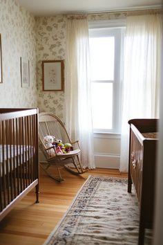 a baby's room with a rocking chair, crib and window in it