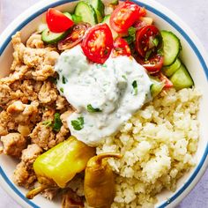 a white bowl filled with rice, meat and veggies next to cucumbers