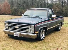 a black pickup truck parked on top of a grass covered field with trees in the background