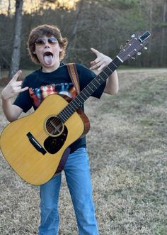 a young man holding an acoustic guitar in his right hand and making a silly face