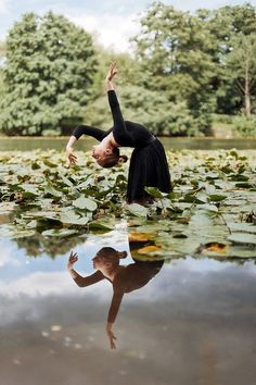 a woman is doing yoga in the water with lily pads on the ground and trees in the background