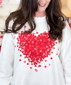 a woman wearing a white sweater with red hearts on the front and back of her shirt