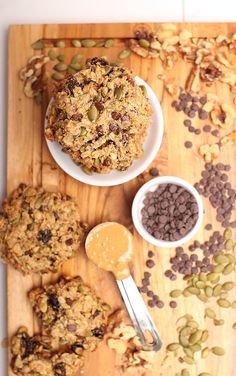 two cookies are on a cutting board next to bowls of nuts and other food items