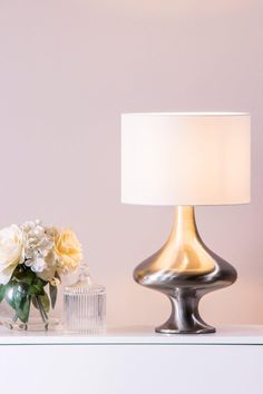 a table with a lamp, vase and flowers on it