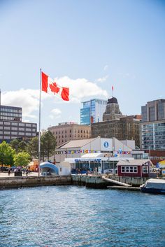 the canadian flag is flying high over the water in front of some buildings and boats