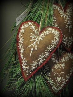 two heart shaped ornaments hanging from a pine tree with needle and thread on it's sides