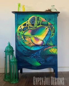 a colorful painted dresser with a turtle on it's front and bottom drawers, next to a green lantern