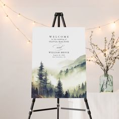 an easel with a welcome sign on it next to a vase and string lights