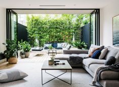 a living room filled with lots of furniture and plants on the wall next to large windows