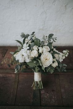 a bouquet of white flowers sitting on top of a wooden table next to a wall