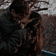 a man and woman kissing in front of trees