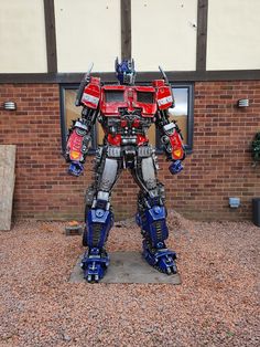 a statue of a transformer standing in front of a brick building with gravel on the ground