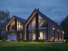 a modern house is lit up at night with lights on the windows and grass in front