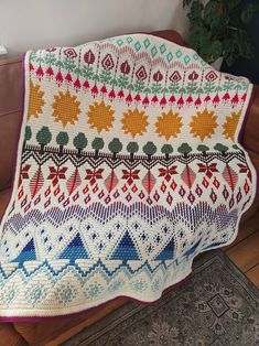 a crocheted blanket sitting on top of a couch next to a potted plant