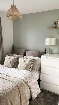 a bed sitting under a window next to a white dresser in a room with gray walls