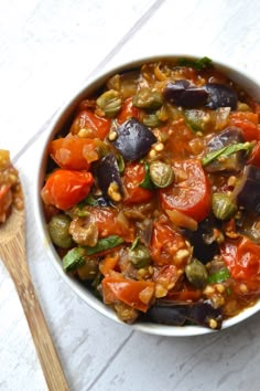 a bowl filled with vegetables next to a wooden spoon on top of a white table