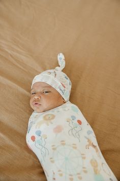 a baby laying on top of a bed wearing a hat