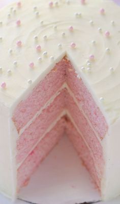 a white cake with pink frosting and sprinkles sitting on a plate