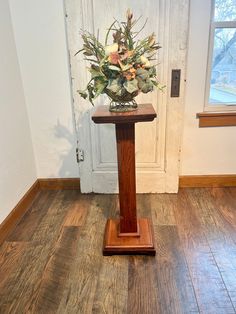 a vase with flowers sitting on top of a wooden stand in front of a door